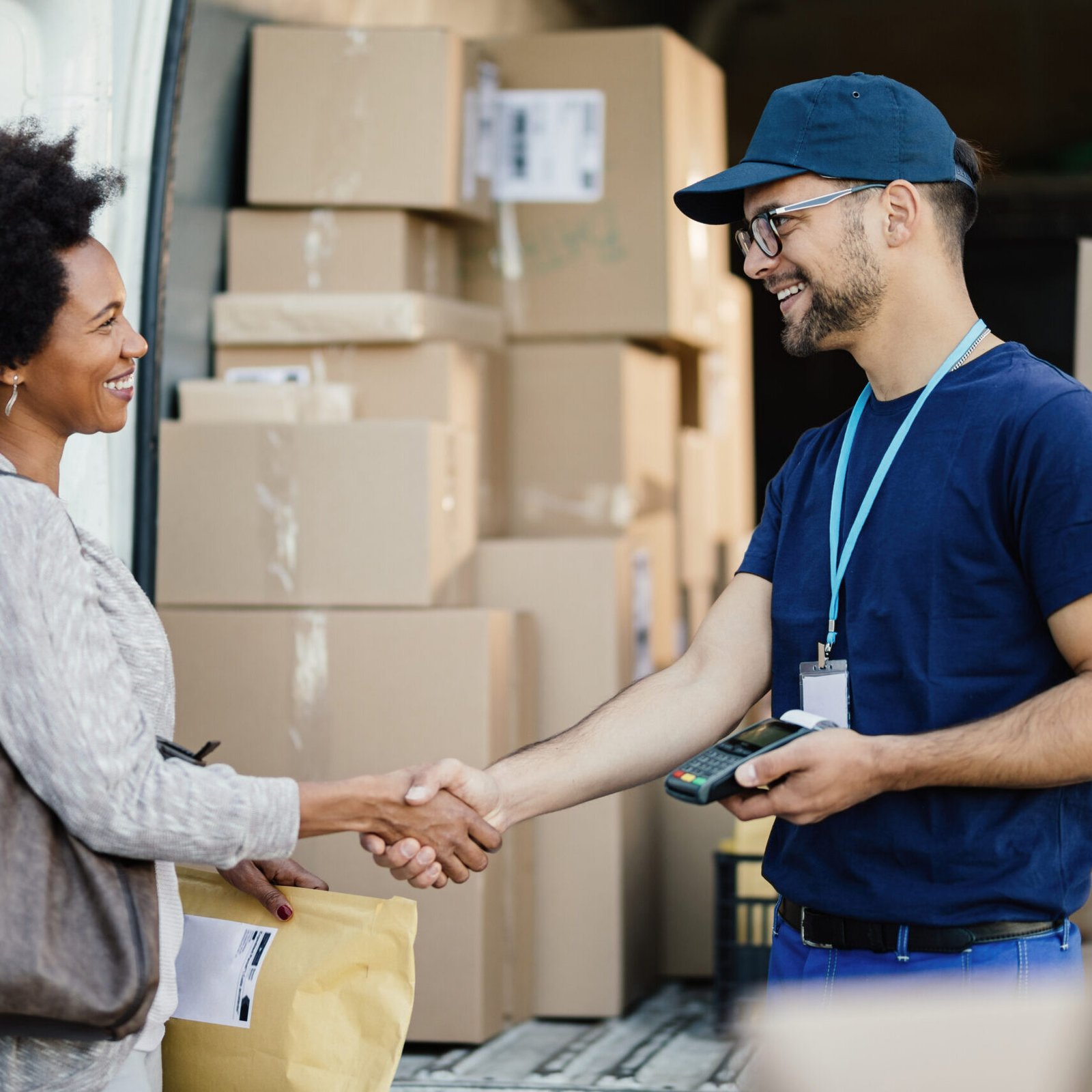 Happy courier handshaking with African American woman while delivering her a package.